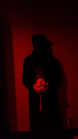 standing ritualist in black robe and black hood holding human skull