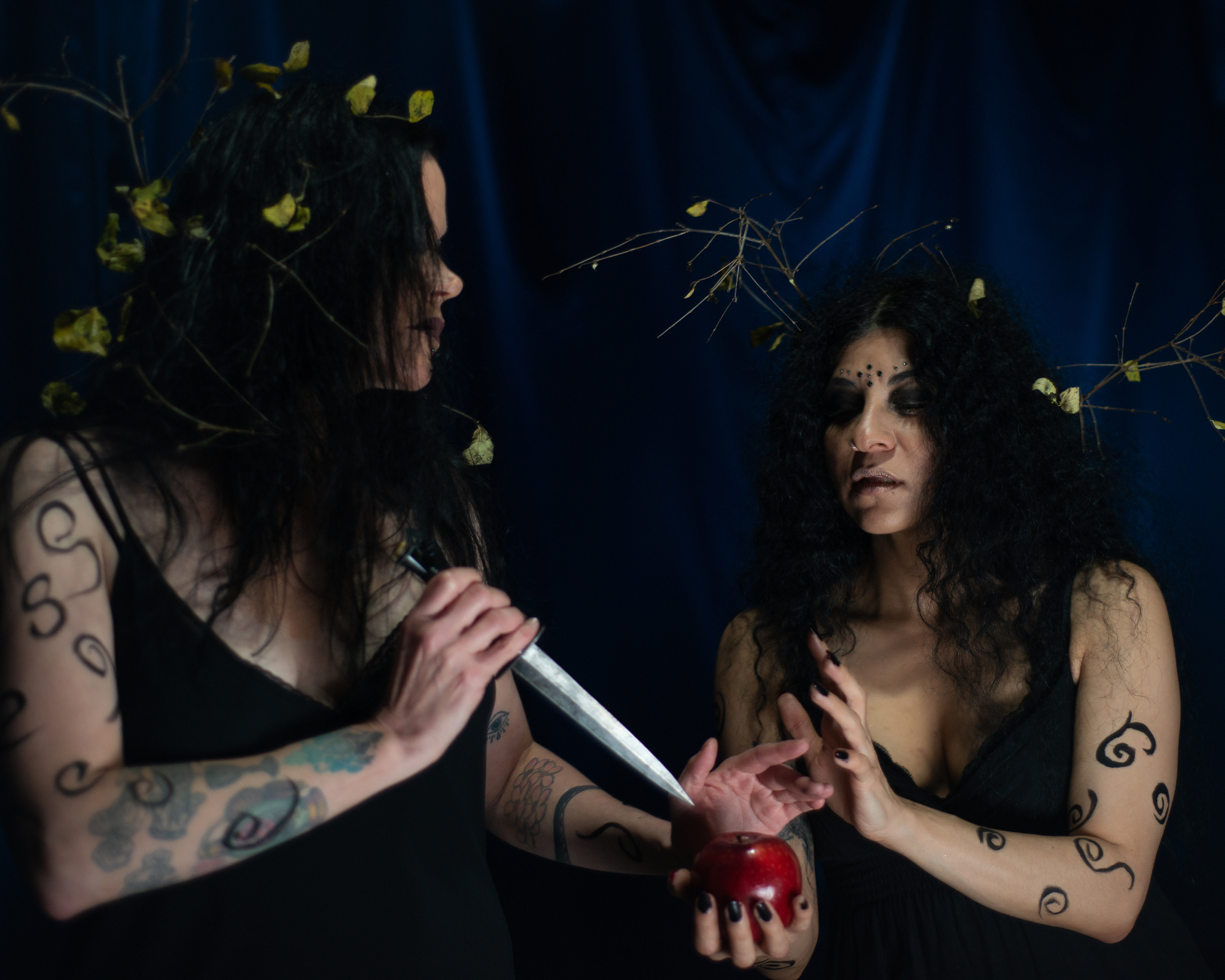 one woman holding an apple, the other hold a ceremonial dagger up to it